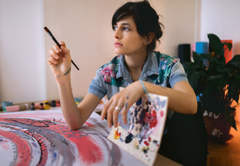 Portrait of female artist with paint brush and palette in studio. Creative activity and inspiration concept. Talented people concept.