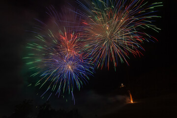 Awesome multi colored explosions of fireworks over trees silhouette and over an illuminated church, Vittorio Veneto, Italy
