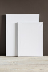 Two white blank canvases of different sizes stand against a dark wall. Mockup. Materials for painting with oil paints and acrylics. Close-up photo.