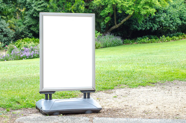 Blank white outdoor advertising stand or sandwich board mockup template. Clear street signage board placed outdoor on the green grass lawn. Background texture of standee in a garden.