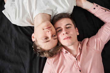 Homosexual boy looking at the camera while laying at the bed with his boyfriend