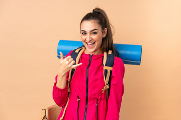 Young mountaineer girl with a big backpacker isolated on beige background making phone gesture