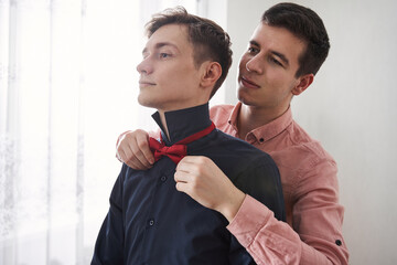 Gay man standing and helping to put on a bowtie to his boyfriend