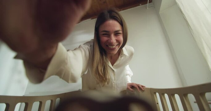 POV shot of young mother giving pacifier to her newborn baby and playing with he while lying in a crib by in a nursery. Concept of family, love,care, parenthood, childhood, life, maternity, motherhood