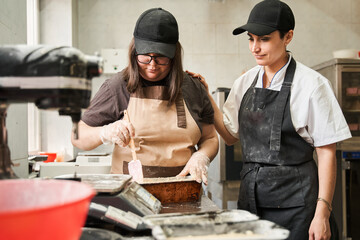 Cook standing at her kitchen table with her assistant and discussing future cake