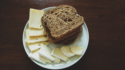 Cheese slices and bread on white plate, wooden table. Flat lay view