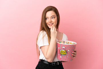 Teenager girl over isolated pink background holding a big bucket of popcorns