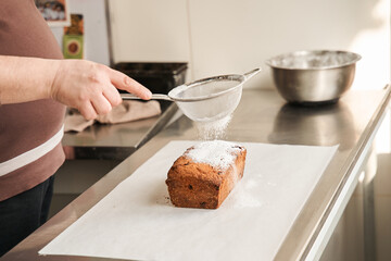 Male baker sprinkling icing sugar over fresh cake