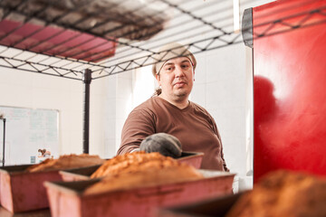Male worker putting cakes in bakeware on tray on a bakery trolley