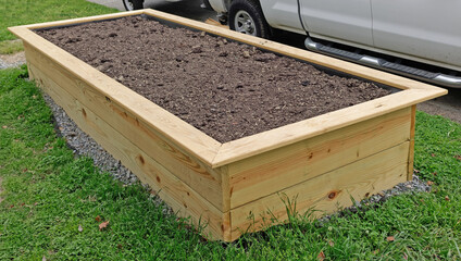 Newly wood constructed raised bed garden box filled with soil.
