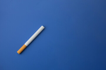 One isolated cigarette with a yellow filter on a blue background. Copy space
