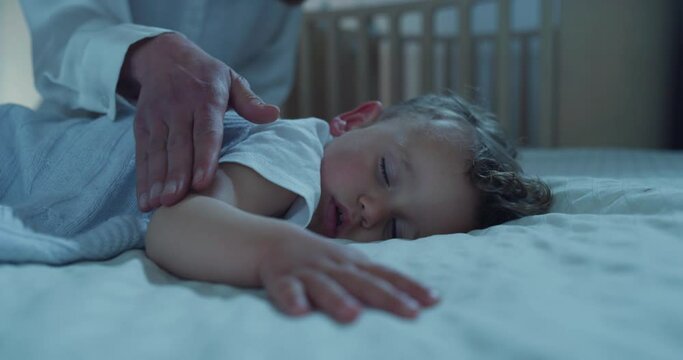 Authentic close up of mother is caressing her toddler baby boy while sleeping by day on bed with soft blanket in a nursery. Concept of family, comfort,care, love, sweet dreams, motherhood, childhood.