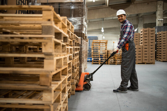 Caucasian warehouse worker lifting weight with manual pallet jack. Working in storage room.
