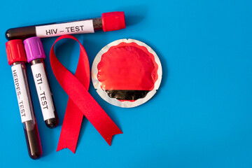 Red AIDS ribbon with blood tubes from sexually transmitted disease tests and a condom on a blue...