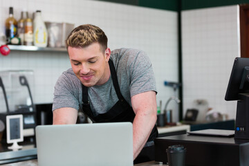 Barista cafe wearing apron and typing laptop computer at coffee shop with happy and smiling.. Worker making coffee on steam espresso coffee machine