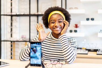 Young woman african american entrepreneur is fashion vlogger show glasses to cellphone and smiling...