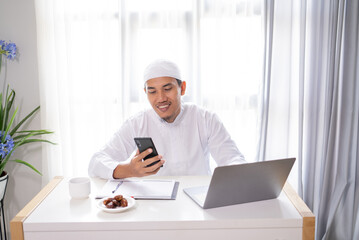busy asian muslim businessman using his smartphone and laptop working from home
