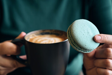 Female hands holding coffee and blue macaroon close-up. Selective focus