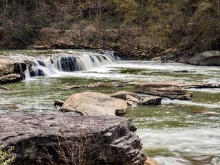 Valley Falls State Park near Fairmont West Virginia in the spring with the multiple waterfalls with cascading water flowing hard through the river and rocks with trees in the background.