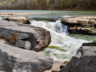 Valley Falls State Park near Fairmont West Virginia in the spring with the multiple waterfalls with cascading water flowing hard through the river and rocks with trees in the background.