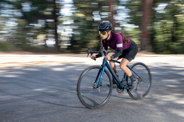 Fototapeta na wymiar Mujer ciclista profesional a toda velocidad en una carretera en medio del bosque. Concepto de triatlón