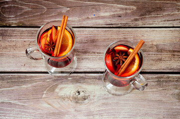Two glasses of fresh mulled wine with orange, apple, cinnamon and anise are on a wooden table.