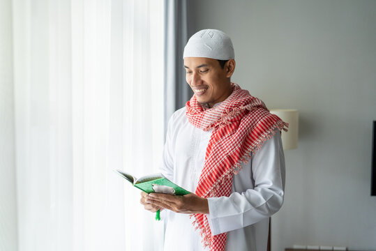 asian religious man reading koran or quran while standing next to the window