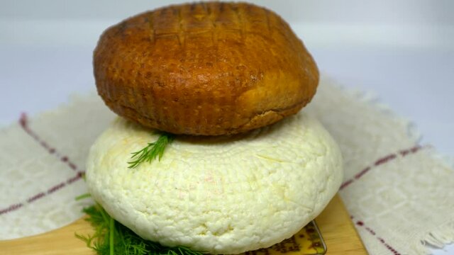 Different types of round soft brown smoked and white homemade cheese. Adyghe cheese with greens lying on wooden board. 4K