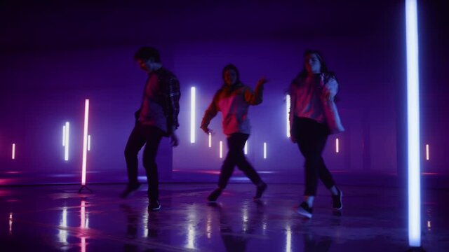 Diverse Group of Three Stylish Professional Dancers Performing a Hip Hop Dance Routine in Virtual Production Studio Environment with 3D Underground Garage Space with Neon Light Lamps.