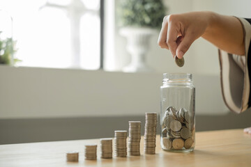 Woman's hand. Put a coin into a glass bottle with coins, saving money with coins, stepping into a successful growing business, and saving for thought in retirement. Retirement savings concept