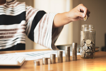 Woman's hand. Put a coin into a glass bottle with coins, saving money with coins, stepping into a successful growing business, and saving for thought in retirement. Retirement savings concept