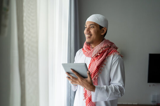 happy muslim businessman smiling while using tablet pc near window