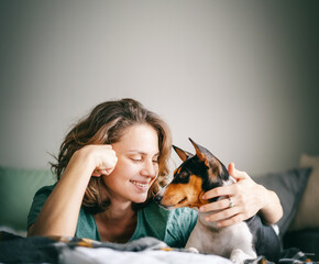Obraz premium Beautiful happy young woman with african terrier bassenji dog on bed hugging tenderly, love pet