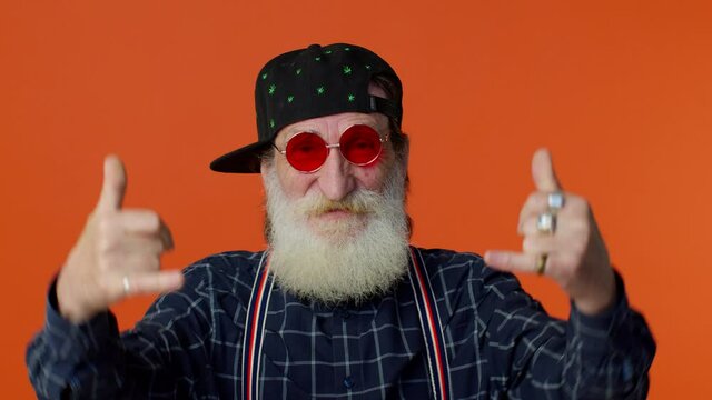 Overjoyed delighted elderly bearded man showing rock n roll gesture by hands, cool sign, shouting yeah with crazy expression, dancing, emotionally rejoicing in success. Senior mature old grandfather