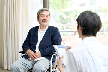 カウンセリング（問診）をする男性介護士と車椅子に乗るシニア男性