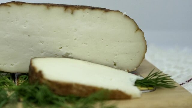 Round soft brown smoked homemade sliced cheese. Adyghe cheese with greens lying on wooden board . 4K