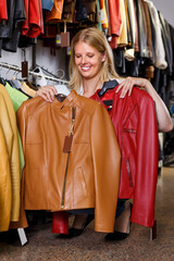 glad young woman choosing stylish leather jacket in clothing store
