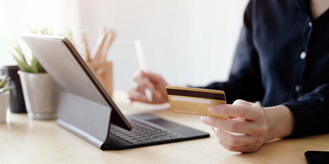 Close up hand of woman holding credit card and using laptop computer at home. Online shopping concept