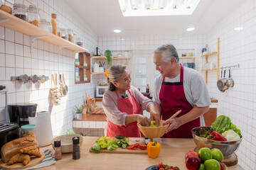 Happy Asian elderly family eating at home. Smiling senior couple enjoy cooking together in the kitchen. Retirement family husband and wife having fun leisure activity lifestyle at home with happiness