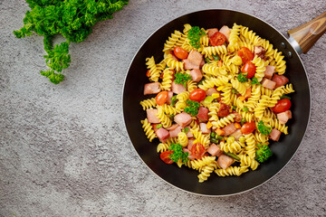 Colorful pasta rotini, cherry tomatoes and ham on pan.