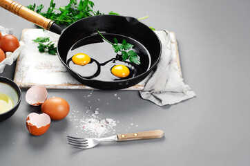 Raw eggs in pan with herbs and seasoning on gray background, prepared food for breakfast.