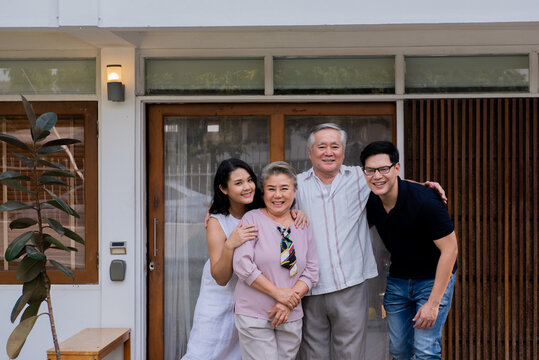 Two-generation Family Standing In Front Of The House Together With Love. Adult Couple Visit To Senior Parents Spending Time Relax And Having Fun On Weekend Vacation Together At Home With Happiness.