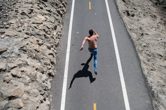 Back view of runner man running jogging on road. Fit male madel workout with bare torso on urban street.