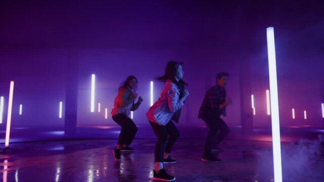 Diverse Group of Three Stylish Professional Dancers Performing a Hip Hop Dance Routine in Virtual Production Studio Environment with 3D Underground Garage Space with Neon Light Lamps.