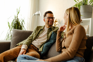 Obraz premium Loving couple sitting on sofa at home. Man and woman relaxing on couch in living room.