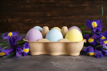 Multi colored Easter eggs in a cardboard box and fresh flower on a wooden background, space for text.