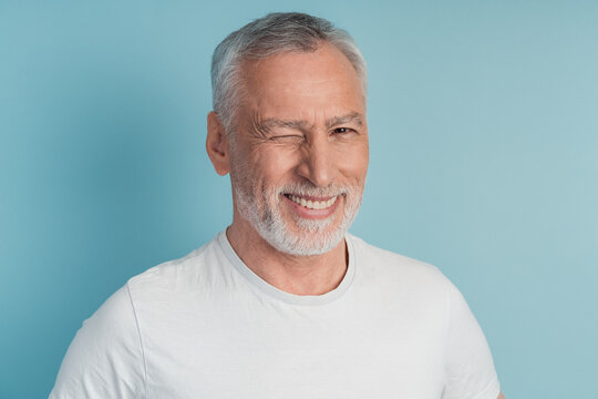 Close up photo of imposing old man winking, enjoying on blue background. Senior man isolated on blank wall background.