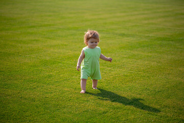 Little baby learning to crawl steps on the grass. Concept childrens months. Happy child playing on green grass playground.