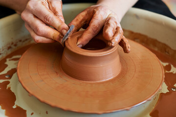 hands of a master potter creating the shape of a bowl on a circle.