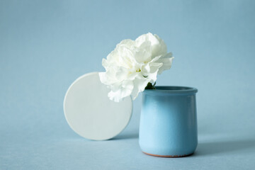 White cocncrete circle shaped pedestal and white flower in vase on blue pastel paper background. Stone platform. Abstract geometric pedestal.